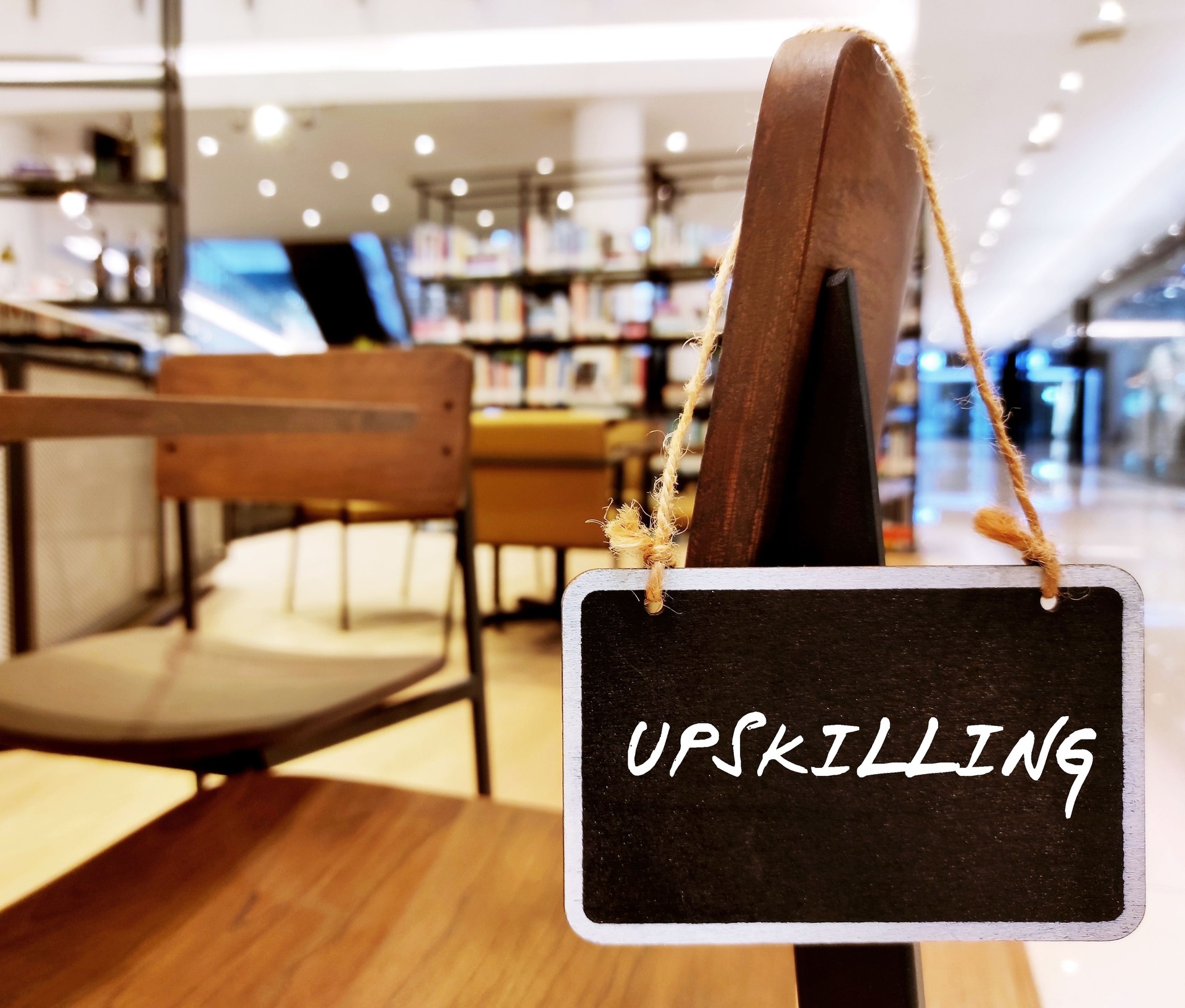 Chalkboard hand on library chair with handwritten text UPSKILLING - the process of learning new skills or of teaching workers new advance skills in organization,train team members continuous education to grow in career path